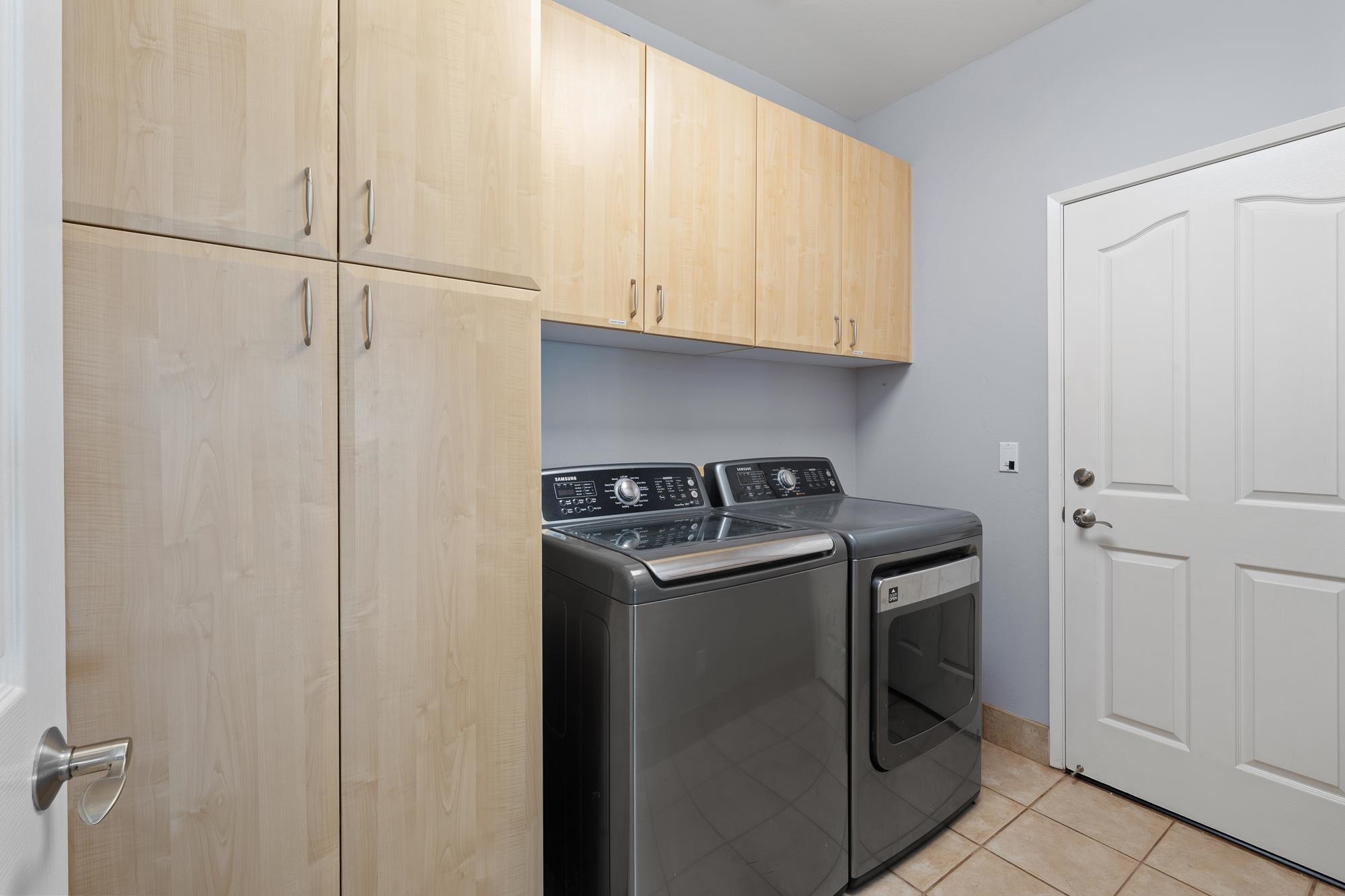 Laundry room with a dark washer and dryer beneath light wood cabinets.