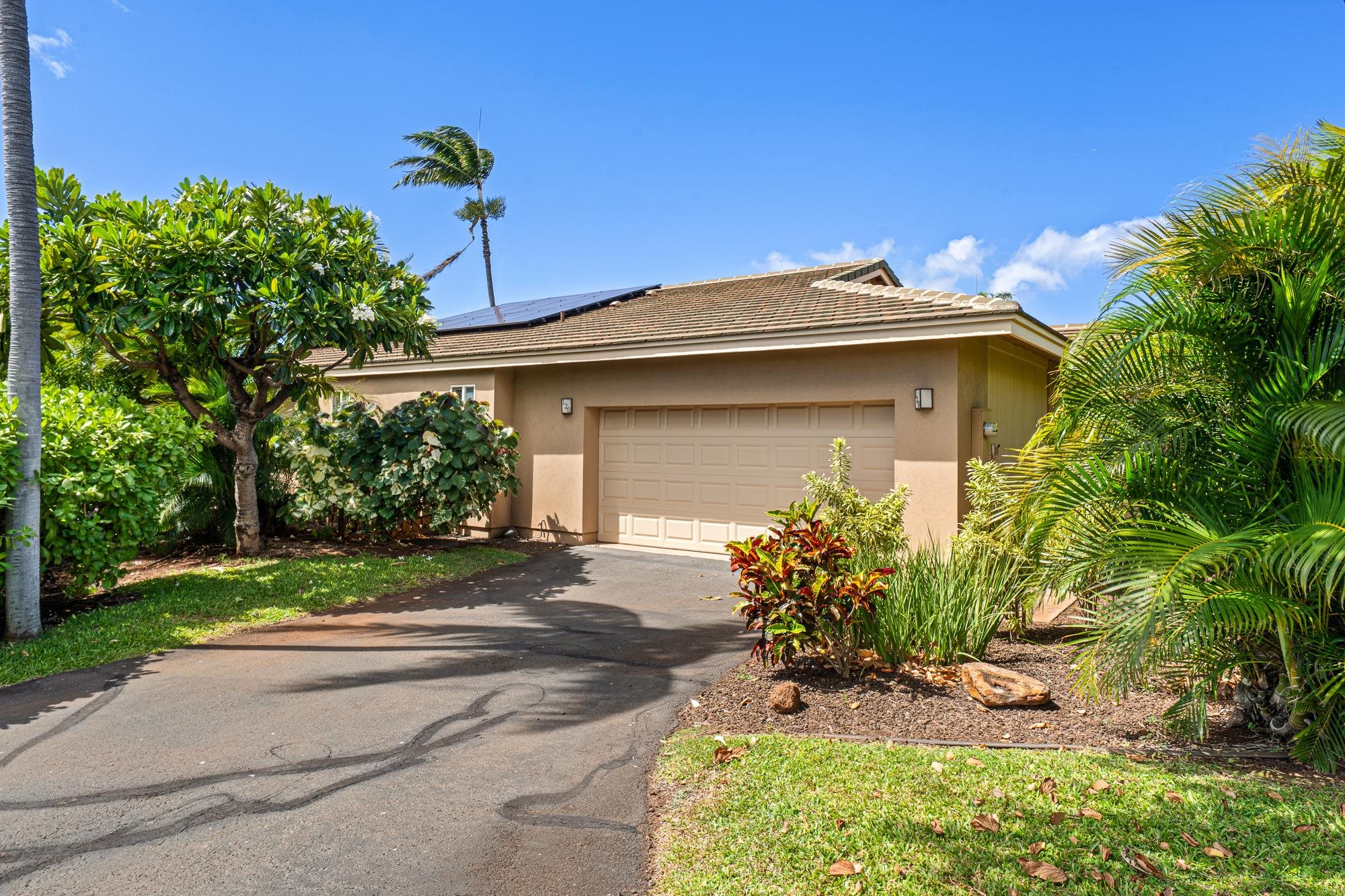 Tan home with solar panels and double garage, framed by lush tropical landscaping.
