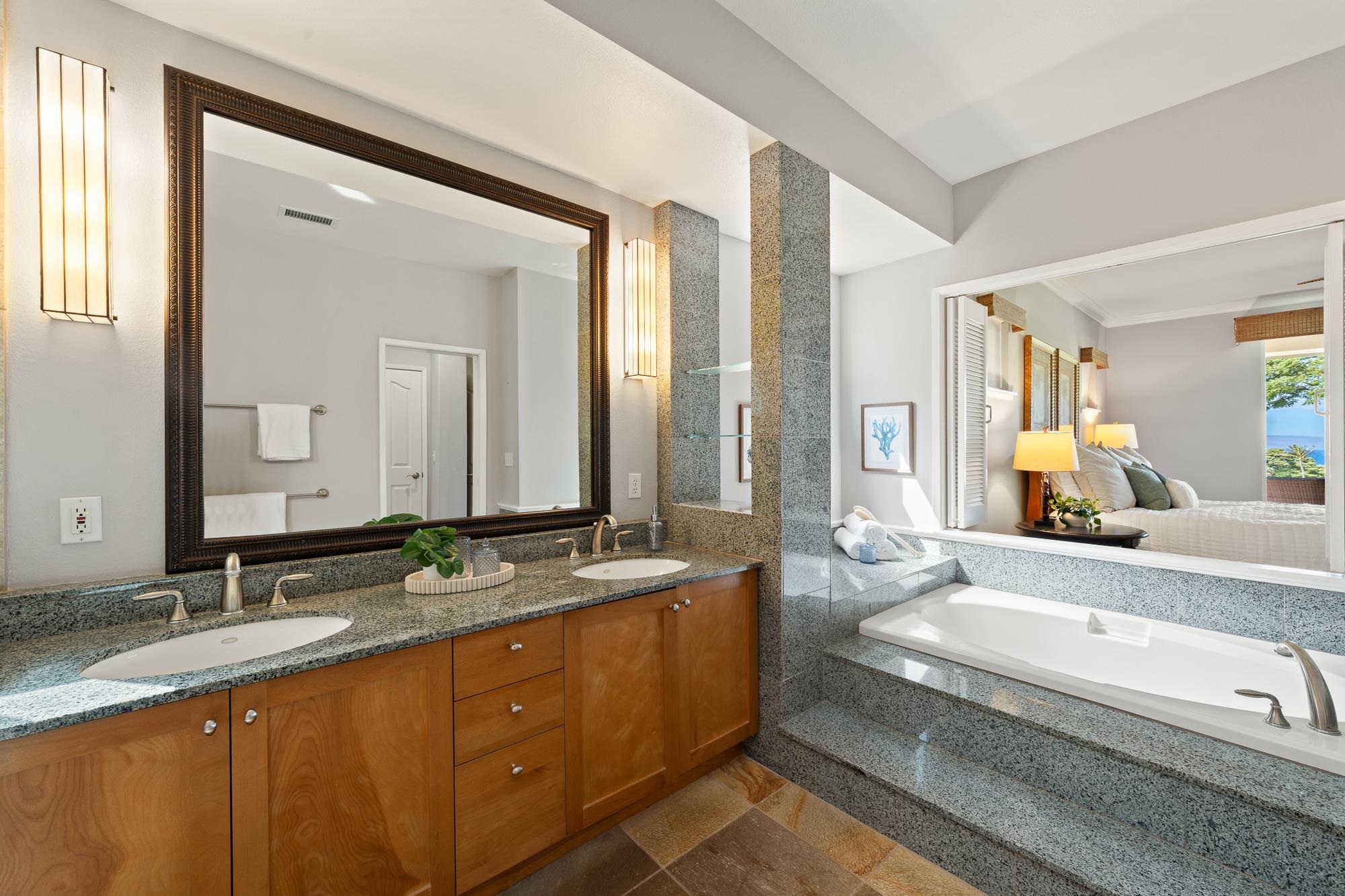 Bathroom with a double vanity and granite soaking tub, opening onto a bedroom with an ocean view.