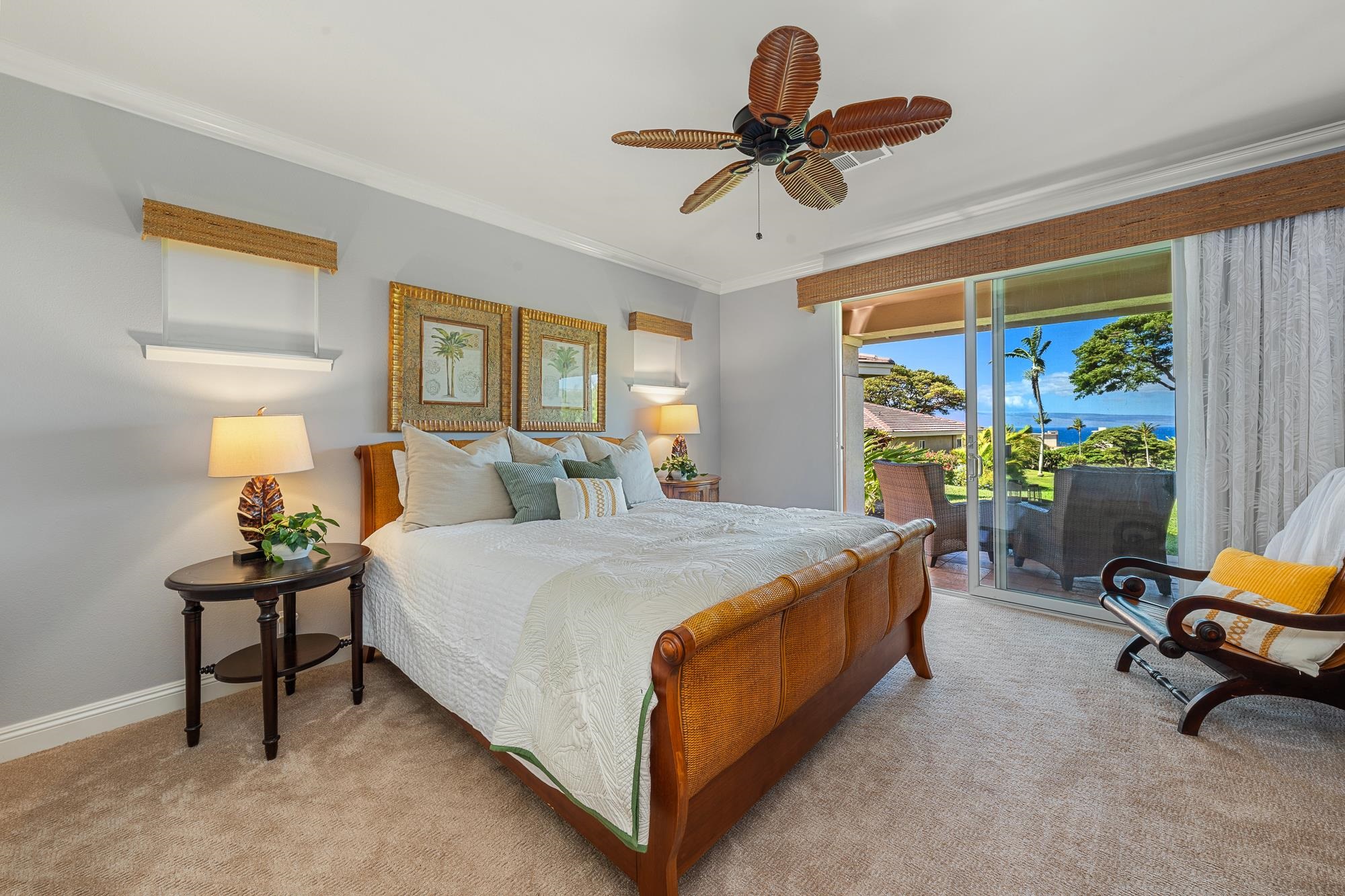 Furnished bedroom with a king bed and sliding doors overlooking a patio, tropical garden, and ocean.