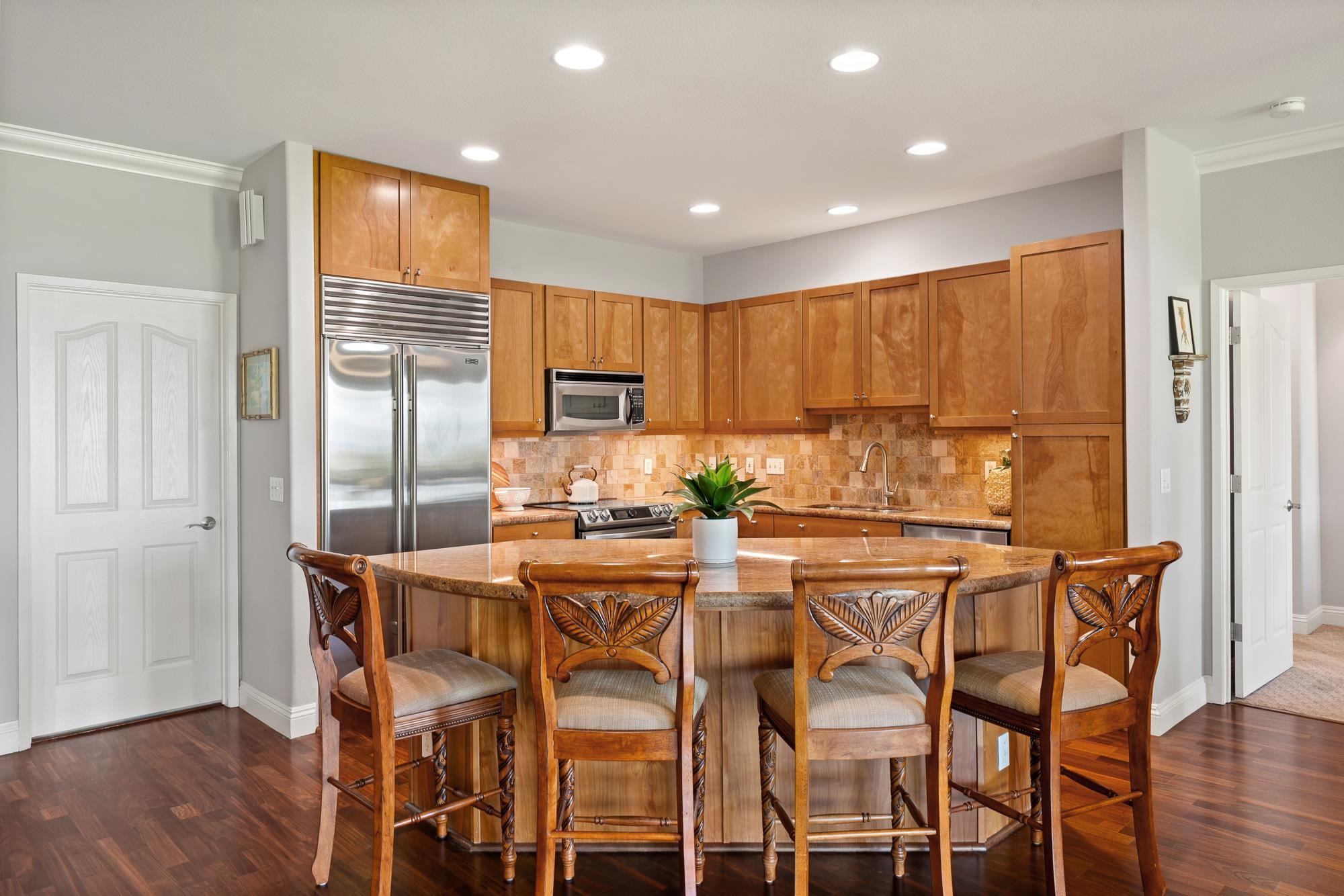 Kitchen with warm wood cabinets, stainless steel appliances, and a granite island with carved chairs.
