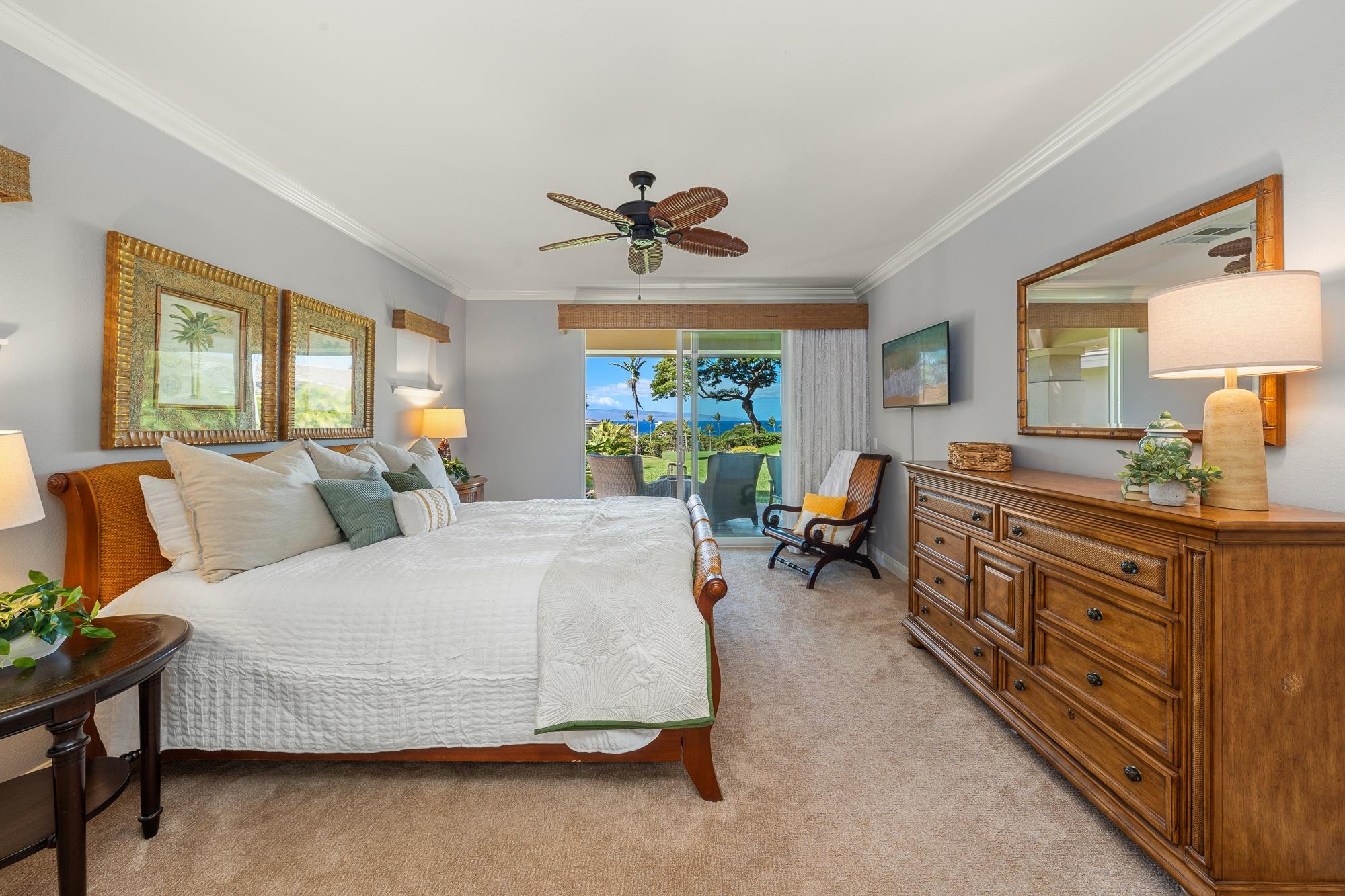 Bedroom with a white-covered bed and wooden furnishings, opening to a garden and ocean view.