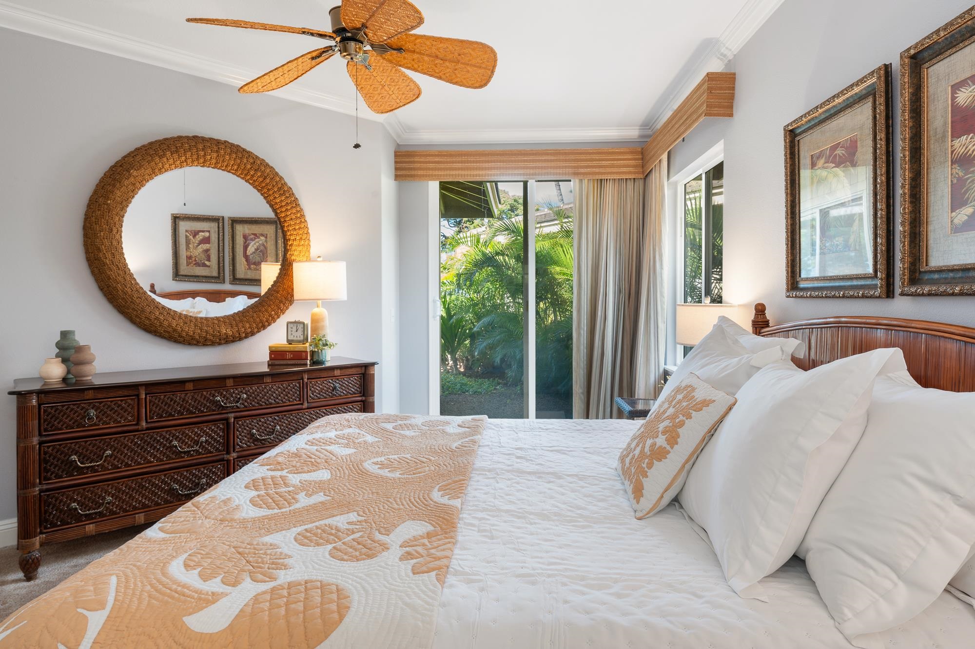 Bedroom with a white bed, rattan mirror and ceiling fan, and sliding doors overlooking tropical greenery.