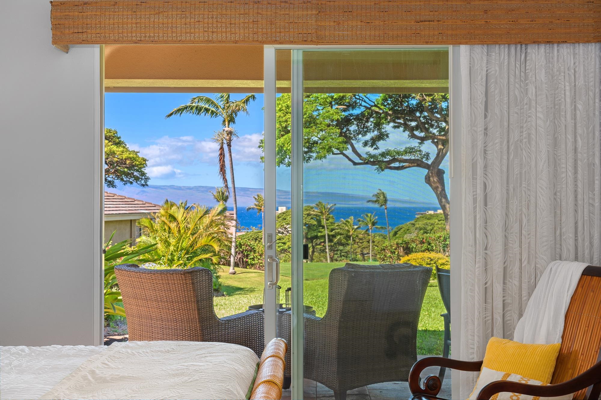 Bedroom with sliding glass doors overlooking a palm-lined garden, ocean, and distant land.