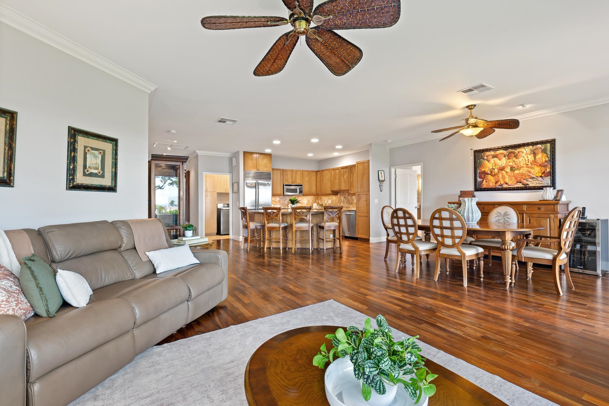 Open-plan living and dining area with wood floors, a gray leather sofa, and a kitchen island.