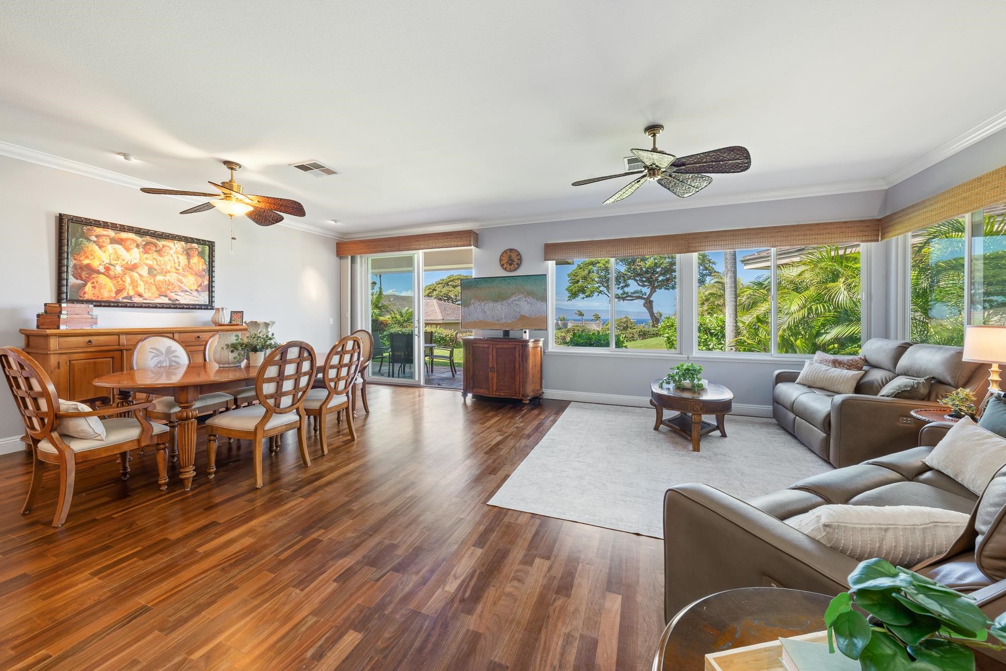 Furnished living and dining room with dark wood floors, ceiling fans, and ocean views through wide windows.