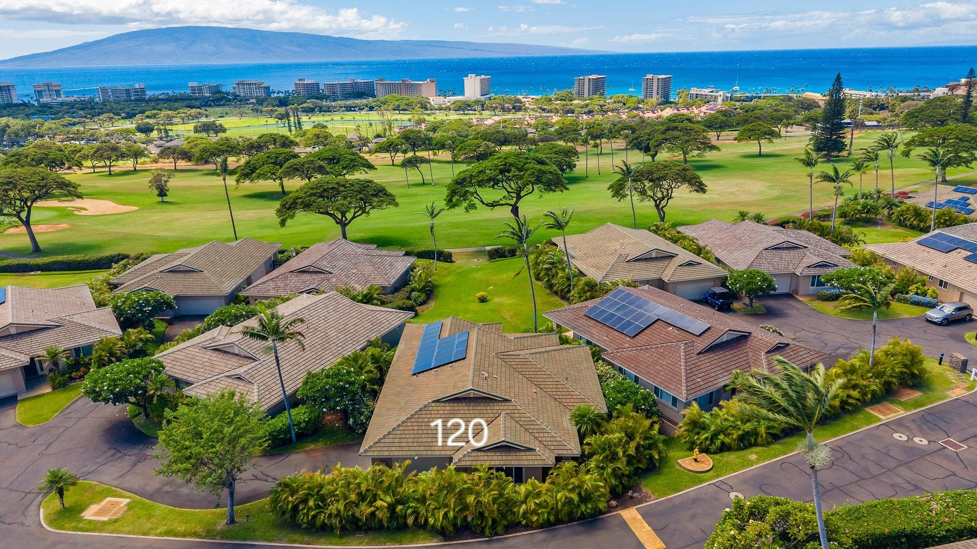 Aerial view of homes beside a golf course, with ocean and island views; 120 marked on a roof.