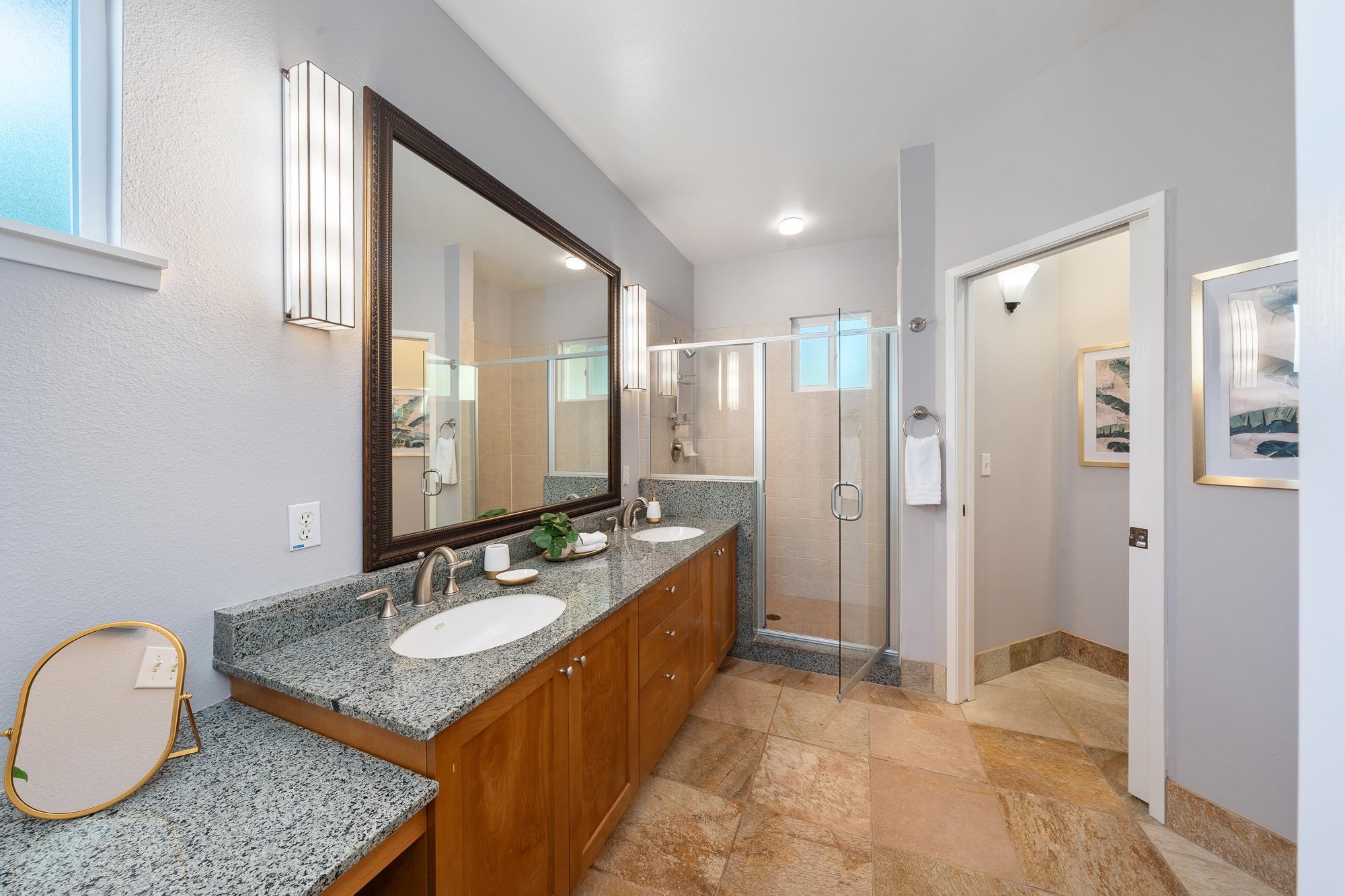 Bathroom with a granite double vanity, warm wood cabinets, and a glass-enclosed tiled shower.