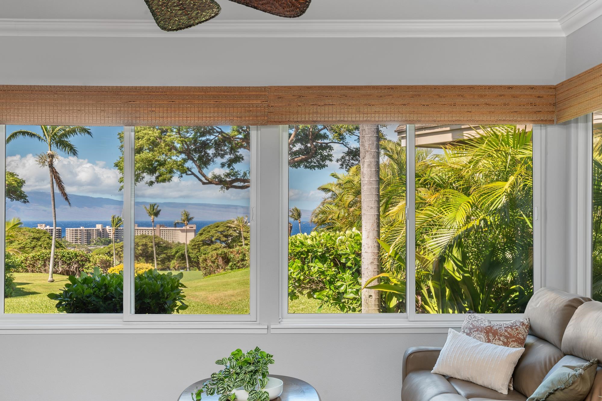 Living room with wide windows overlooking tropical gardens and ocean, with a leather sofa beside the view.