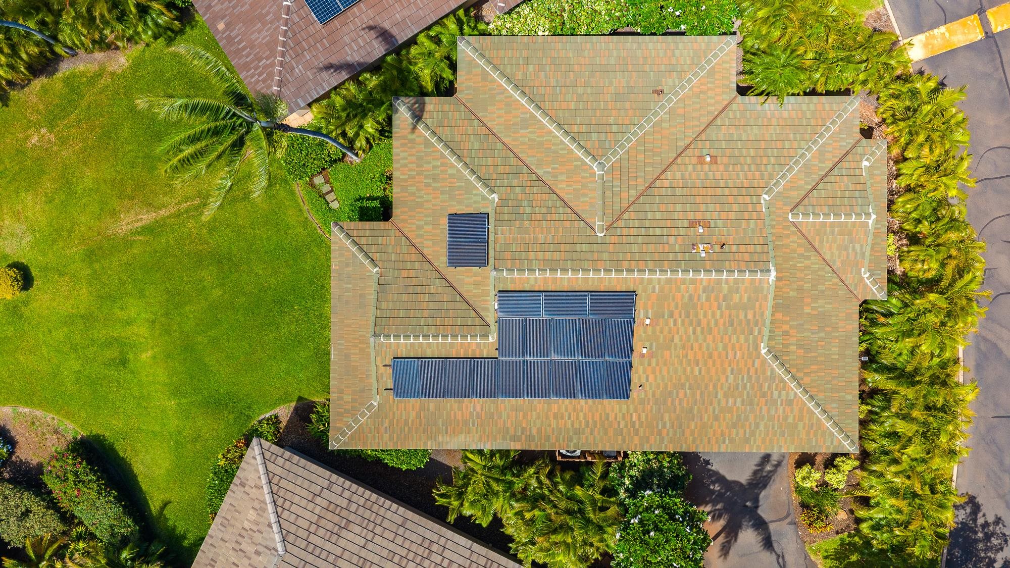 Aerial view of a tiled-roof home with solar panels, beside a broad lawn and palm trees.