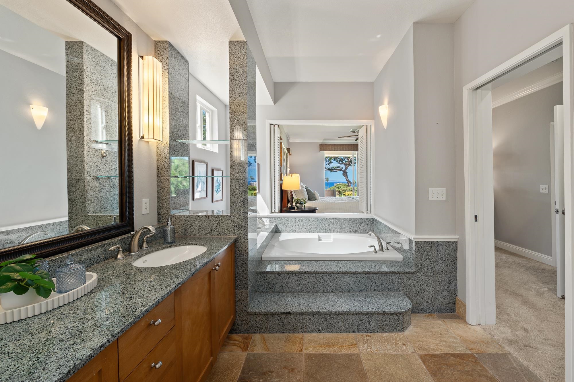Bathroom with granite vanity and built-in soaking tub, looking through to a bedroom and ocean view.