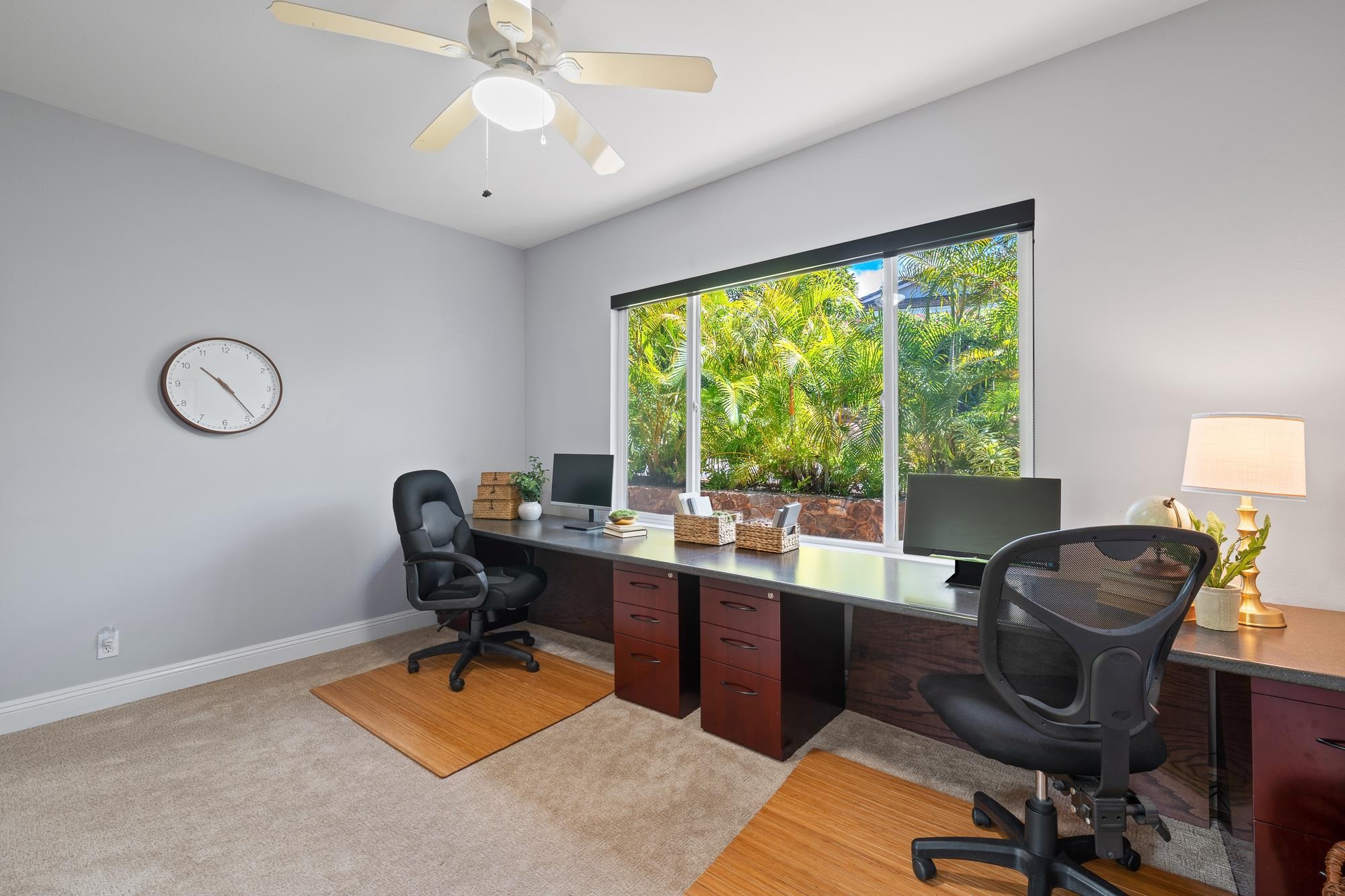 Home office with two desk setups and a large window overlooking tropical palms.