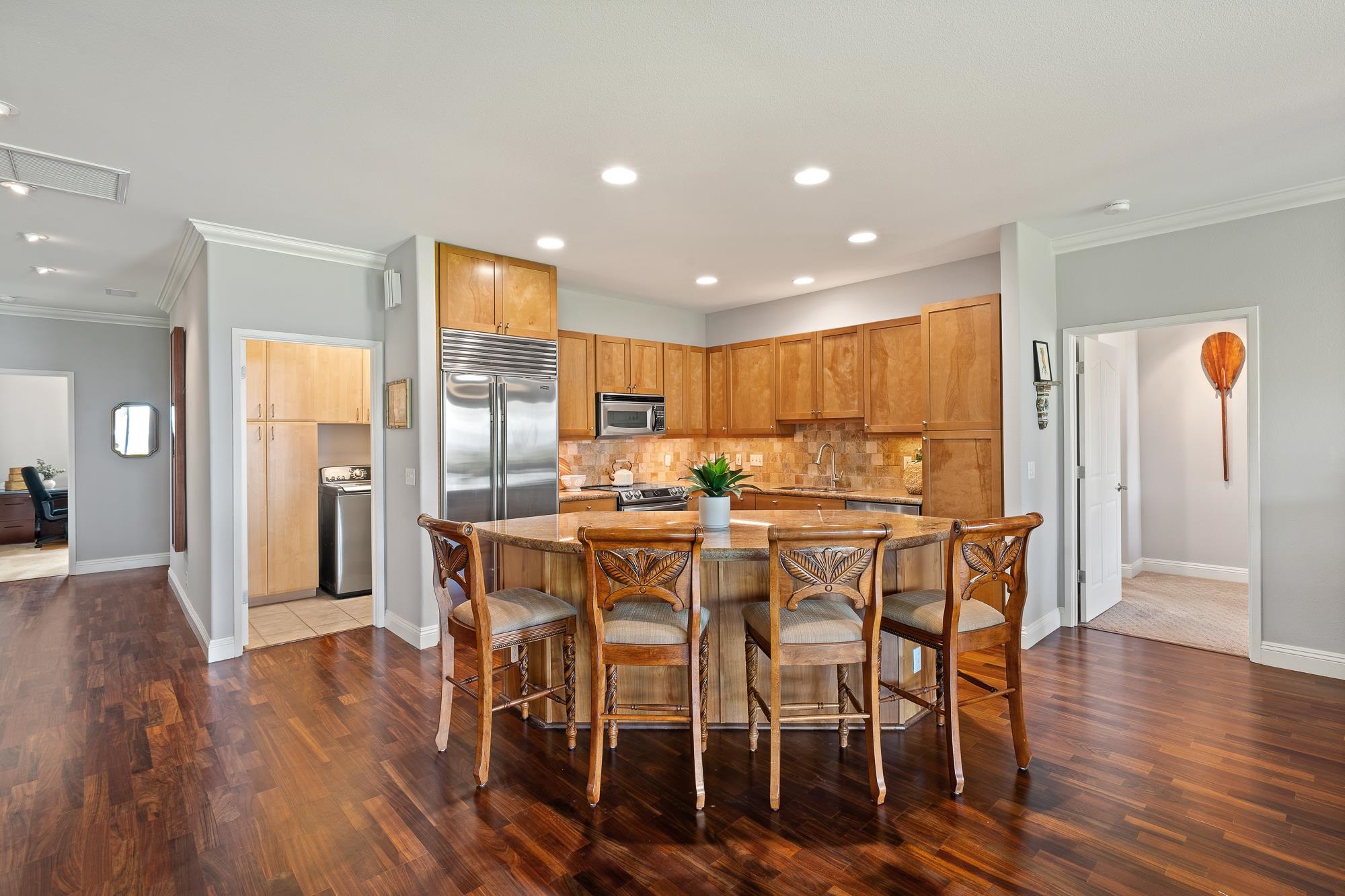 Open kitchen with wood cabinets, stainless appliances, and a stone island surrounded by carved bar stools.
