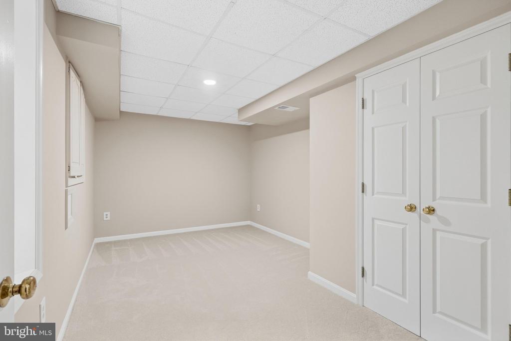 Empty finished room with beige carpet, white double closet doors, and a suspended tile ceiling.