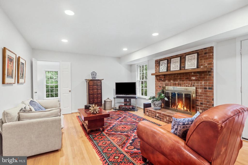 Living room with brick fireplace, hardwood floors, patterned rug, and cream and leather seating.