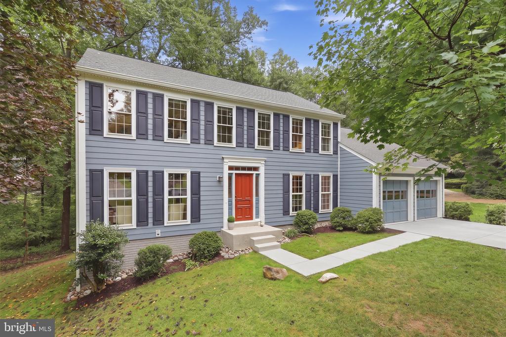Two-story blue-gray house with a red front door, attached garage, and mature trees.