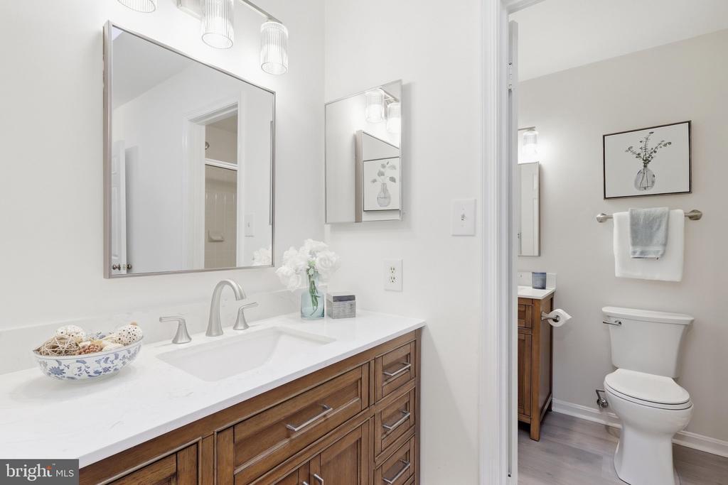 Bathroom with a wood vanity, white countertop, large mirror, and adjoining toilet area.