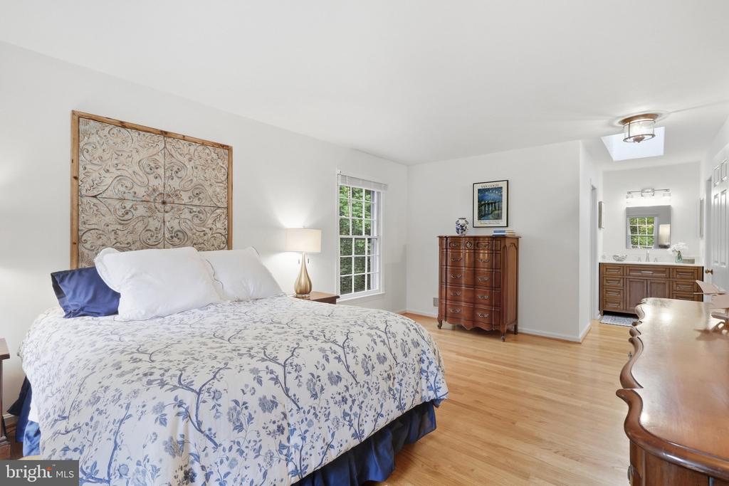 Bedroom with a floral-quilted bed, ornate headboard, hardwood floors and adjoining bathroom.