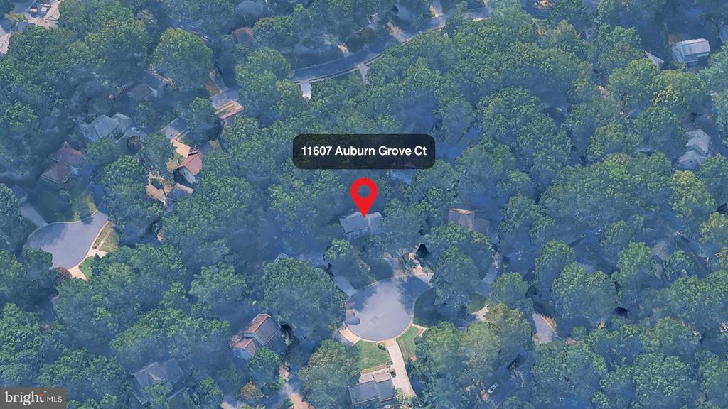 Aerial view of a wooded neighborhood with a red pin marking 11607 Auburn Grove Court near a cul-de-sac.
