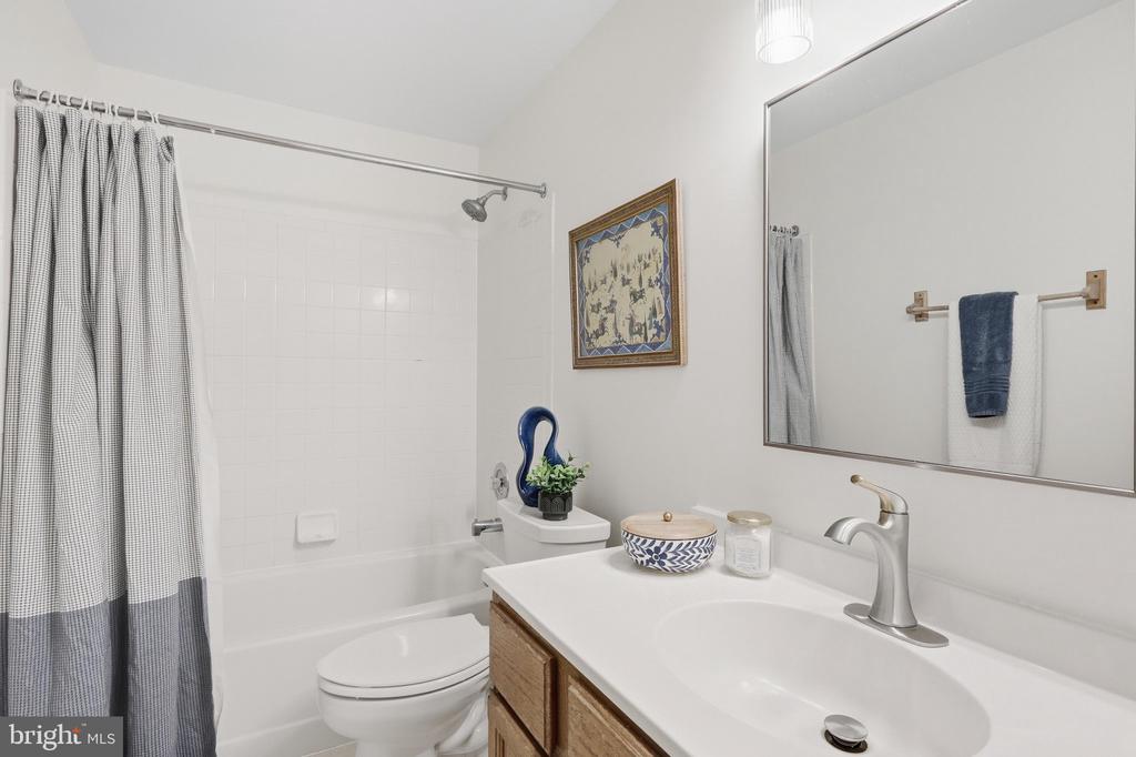Bathroom with white tub, striped shower curtain, toilet, and wood-cabinet vanity.