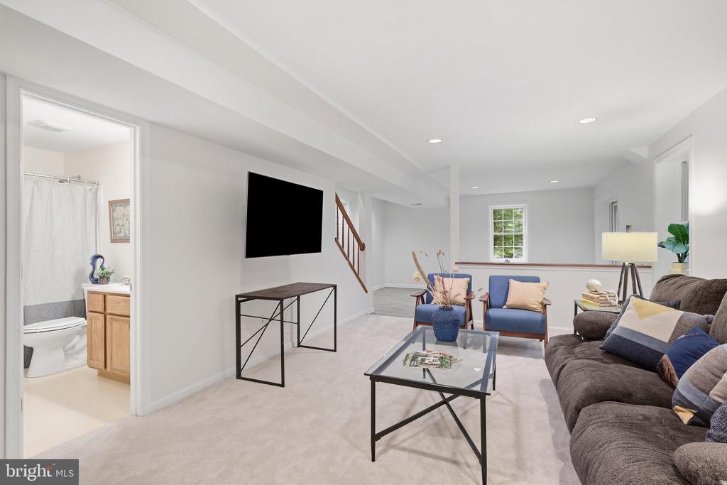 Lower-level family room with a brown sectional, blue armchairs, glass coffee table, and wall-mounted television.