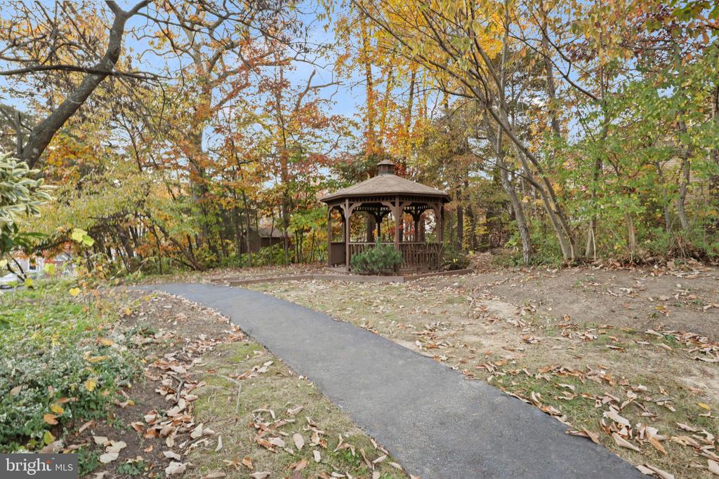 Wooden gazebo beside a paved path beneath autumn trees.