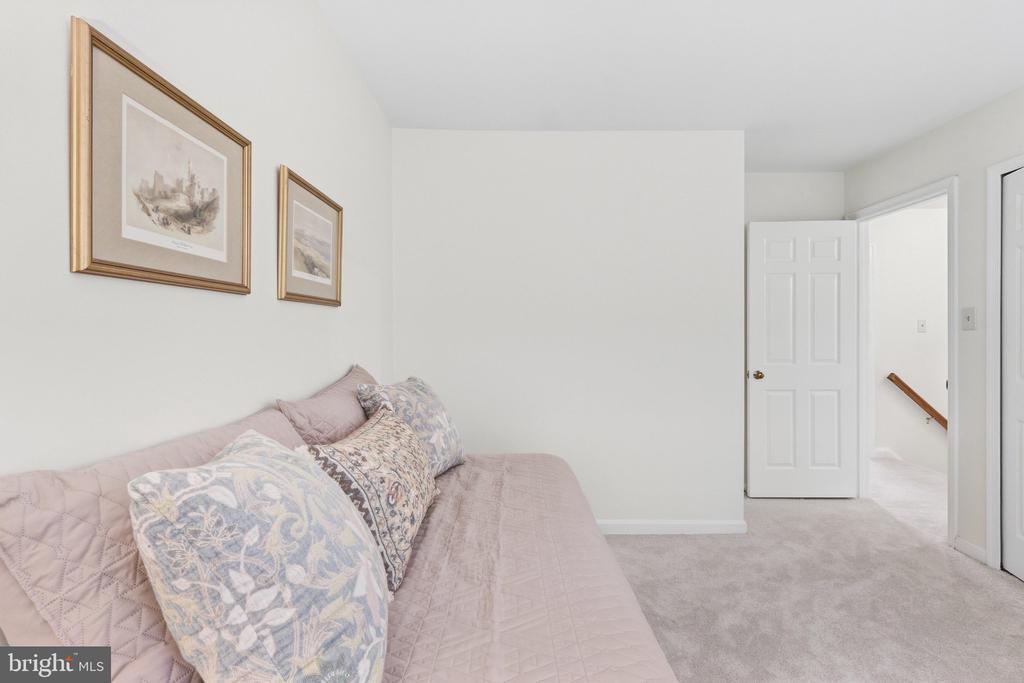 Bedroom with a pale pink quilted bed, patterned pillows, and framed artwork.