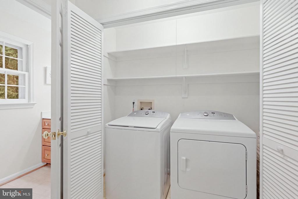 Laundry room with washer and dryer beneath open shelves and louvered doors.