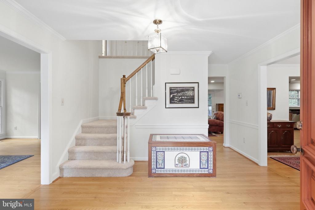 Foyer with carpeted staircase, hardwood floors, and a decorative tiled chest.
