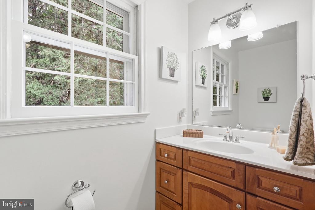 Bathroom with a warm wood vanity, large mirror, and window overlooking leafy trees.