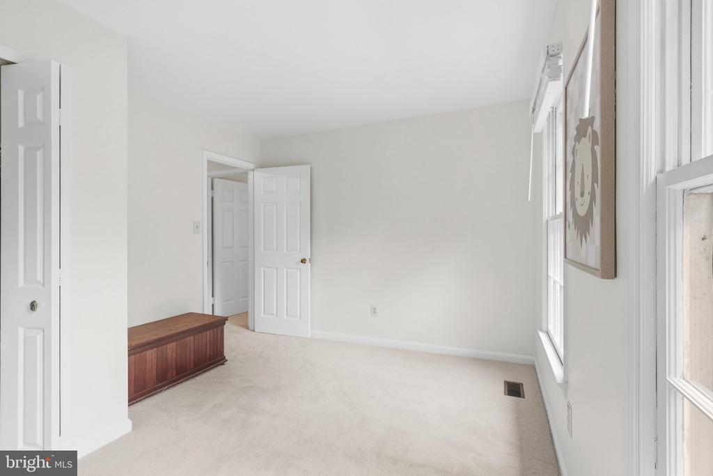 Empty carpeted bedroom with two windows, an open door, and a low wooden chest.