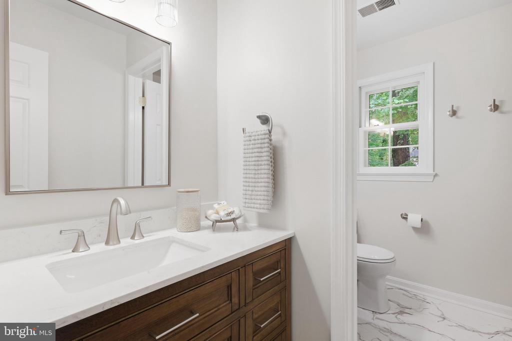 Bathroom with a dark wood vanity, white sink, large mirror, and separate toilet area.