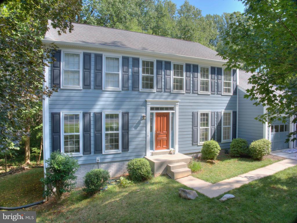Two-story blue-gray house with dark shutters, an orange front door, and an attached garage.