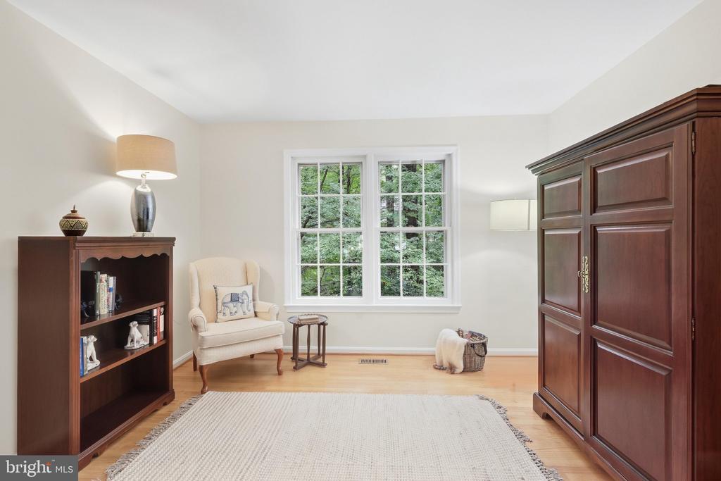 Furnished sitting room with a large garden-facing window, upholstered chair, and dark wood armoire.