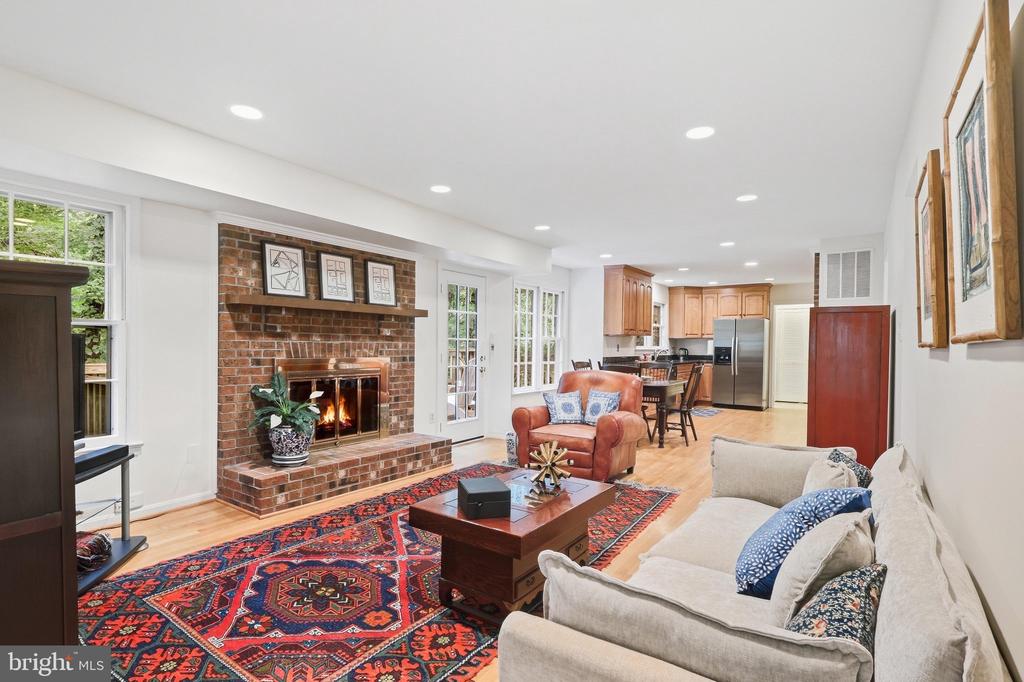 Open-plan living room with a brick fireplace, colorful rug, and kitchen beyond.