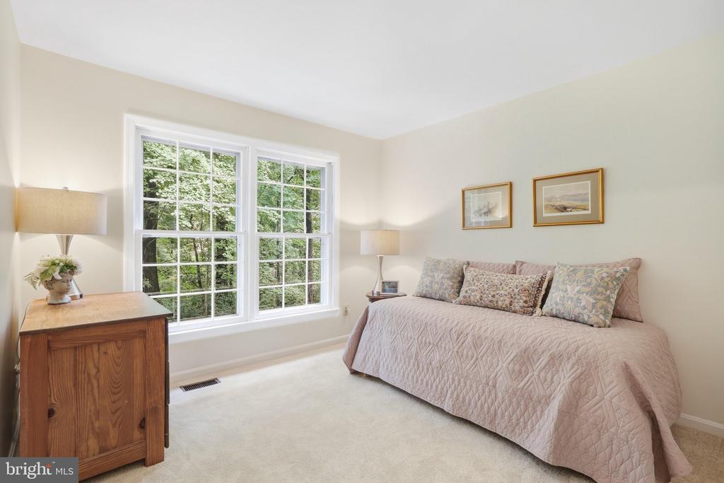 Bedroom with a quilt-covered bed and large windows overlooking leafy trees.