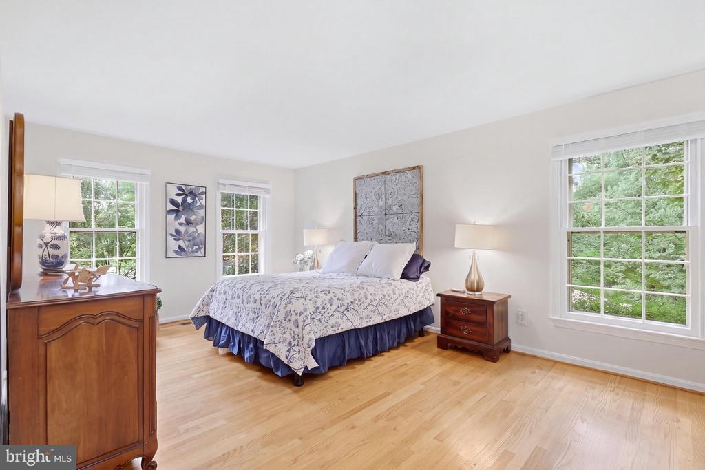 Furnished bedroom with patterned bedding, hardwood floors, and three large windows overlooking greenery.
