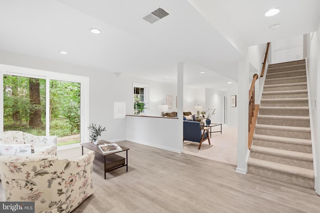 Open-plan living area with floral armchairs, wooded views through glass doors, and a carpeted staircase.