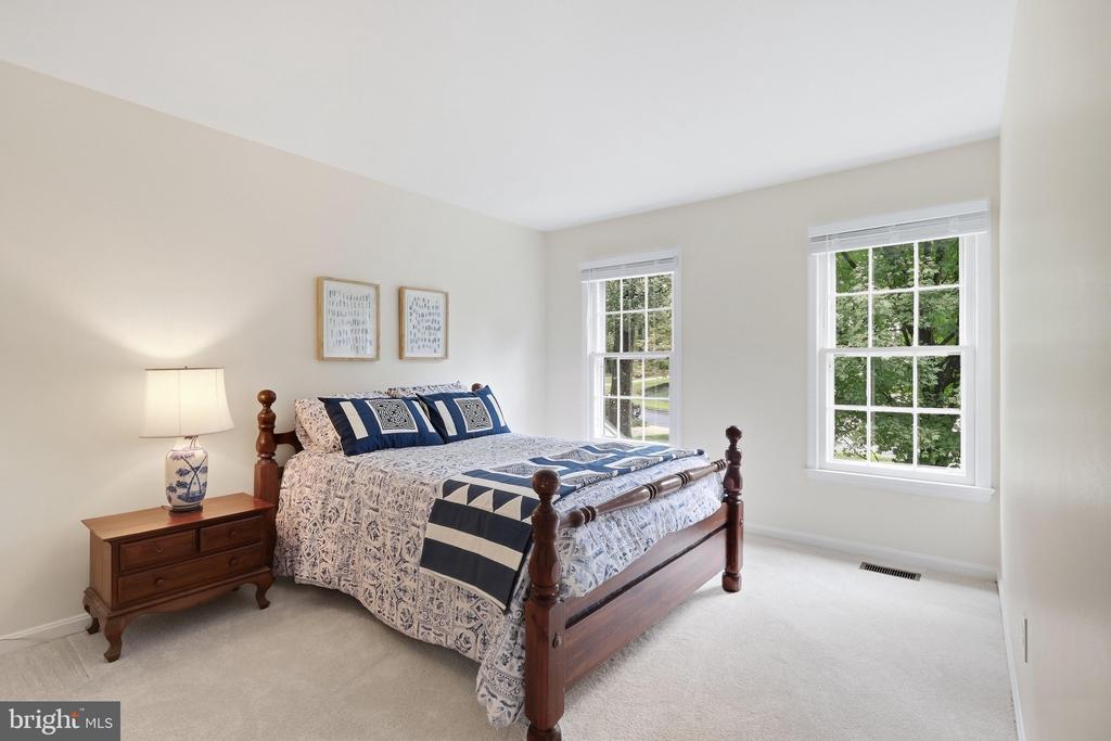 Bedroom with a dark wood four-poster bed, blue-and-white bedding, and two windows overlooking greenery.