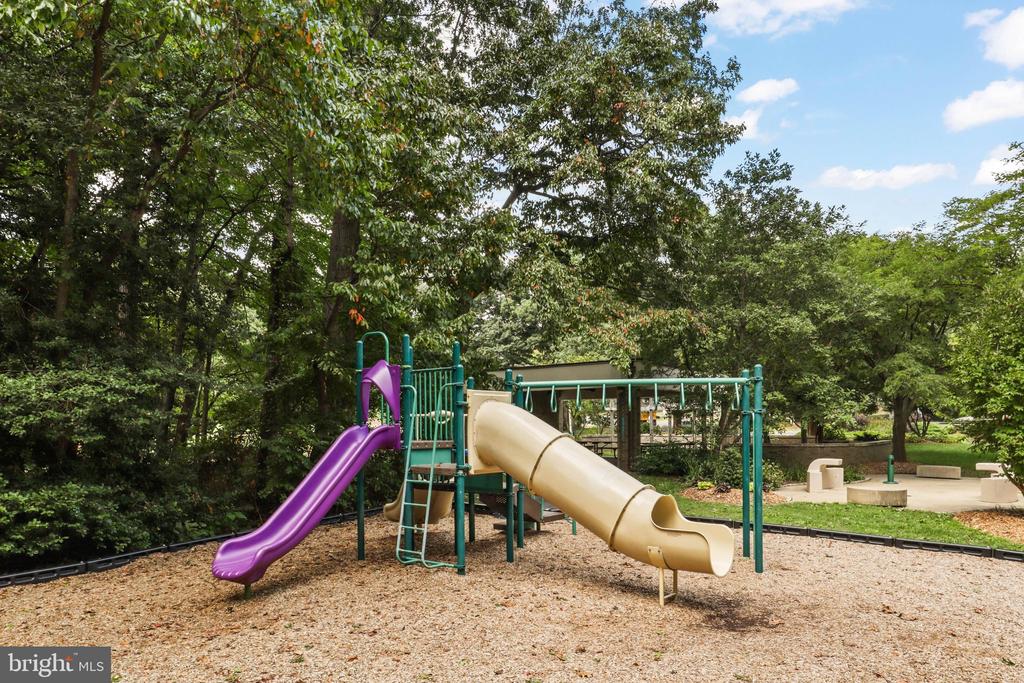 Community playground with purple and tan slides beneath mature trees.