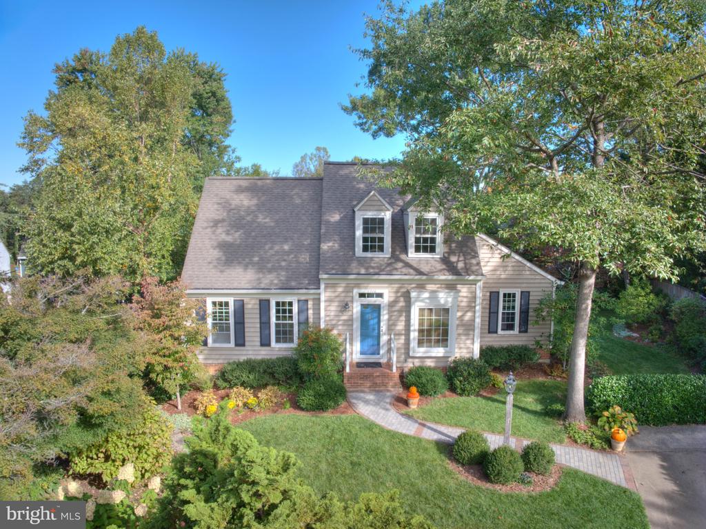 Front exterior of a beige home with a blue door, dormer windows, and landscaped yard.
