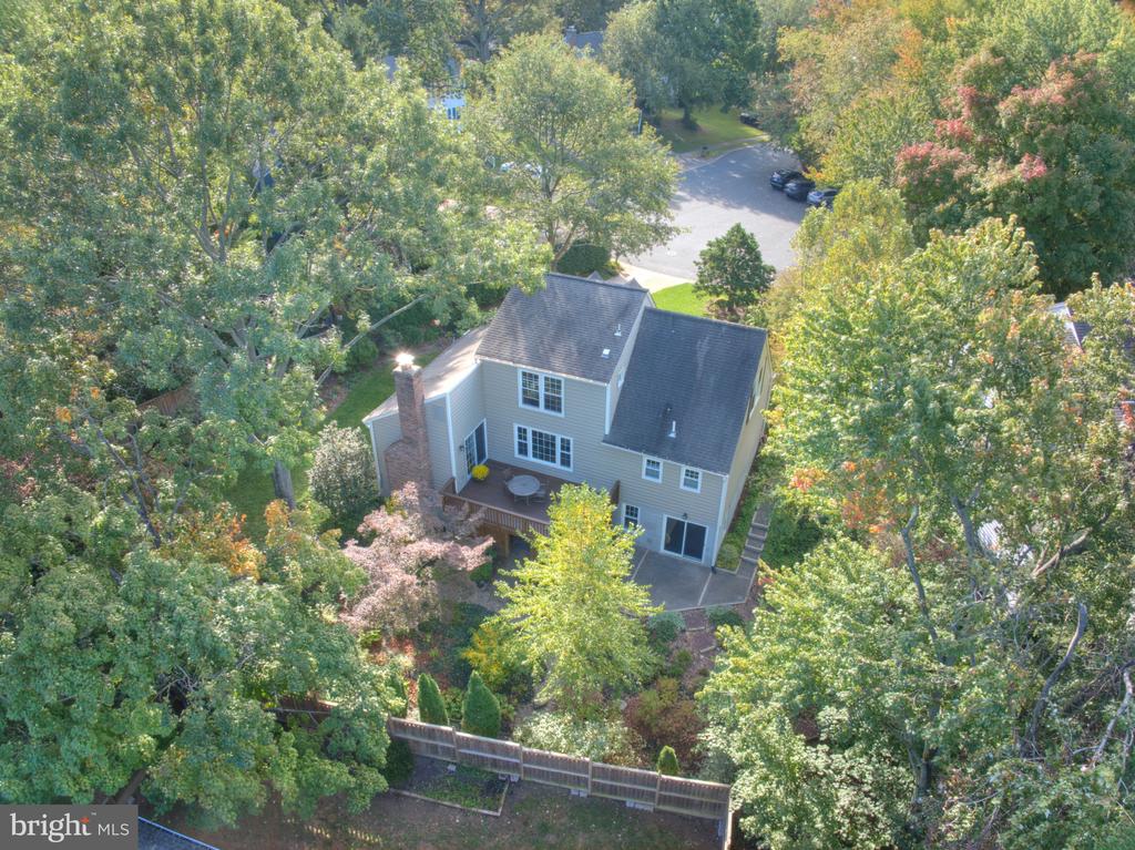 Aerial view of a two-story home's wooded backyard, deck, and fenced lot.