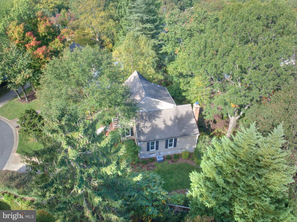 Aerial view of a gray-sided home surrounded by mature trees and landscaped grounds.