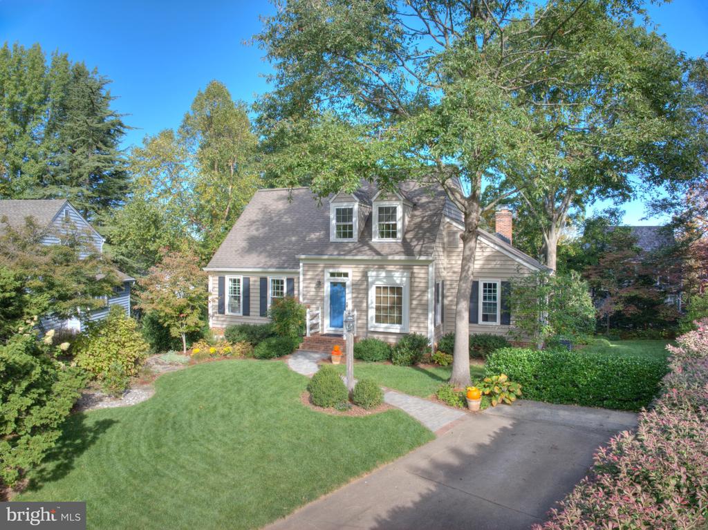 Cape Cod home with a blue front door, two dormers, and a landscaped lawn beneath mature trees.