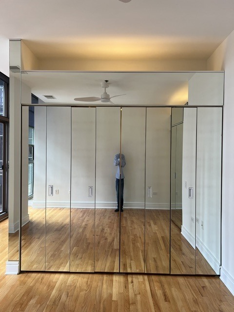 Bedroom with mirrored closet doors, hardwood floors, and a ceiling fan.