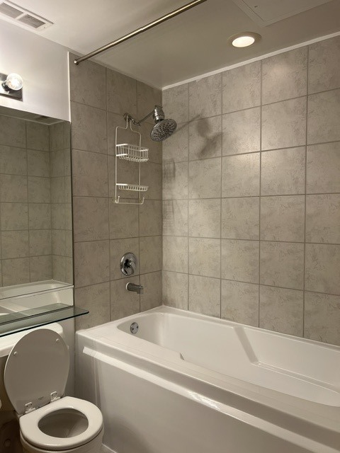 Bathroom with a white bathtub, tiled shower walls, and a toilet beside a mirrored vanity.