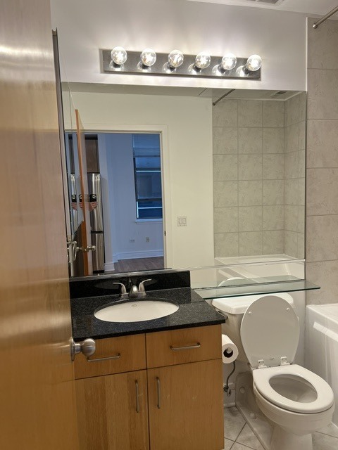 Bathroom with wood vanity, granite countertop, toilet, and tiled tub surround.