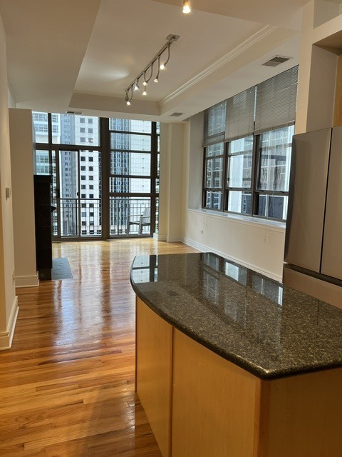 Open condo living area with hardwood floors, large city-facing windows, and a granite kitchen island.