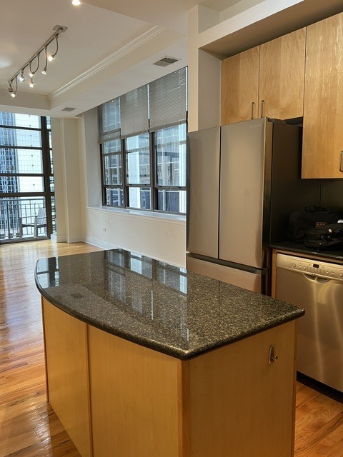 Open kitchen with a granite-topped island, wood cabinets, and large windows overlooking nearby buildings.