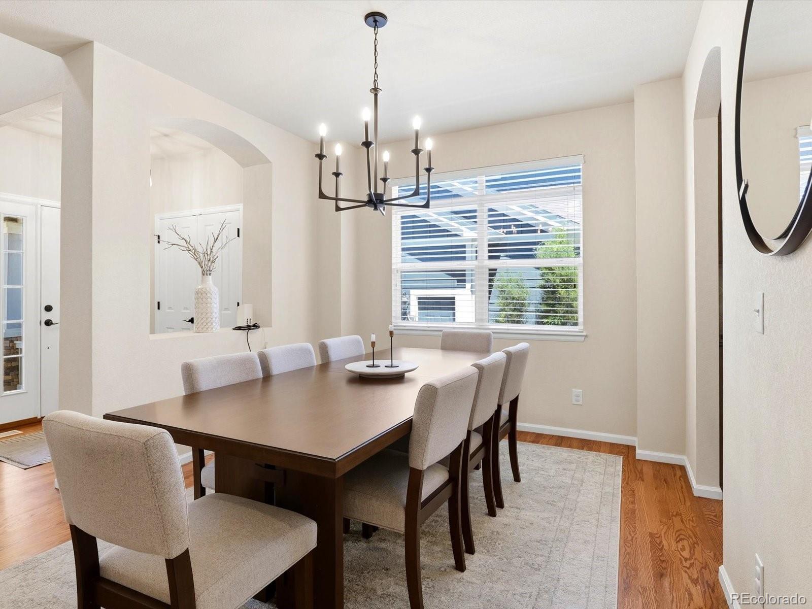Dining room with a dark wood table, upholstered chairs, and a modern chandelier beside a large window.